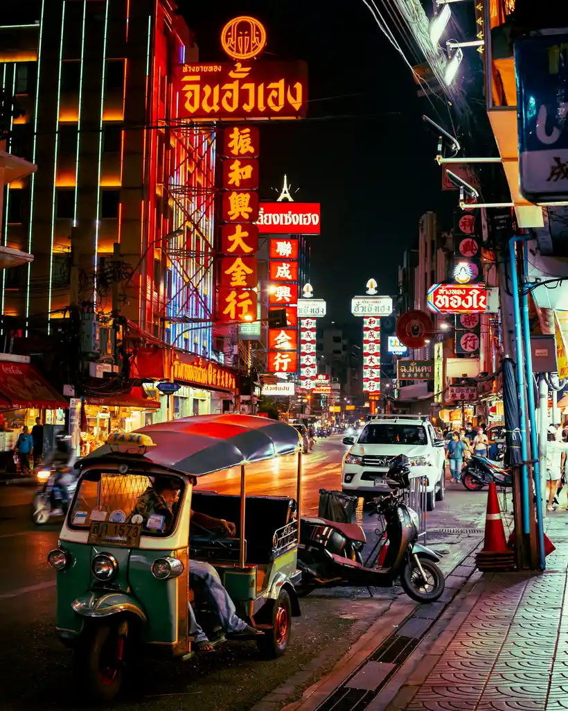 Yaowarat nightlife with neon signs, tuk-tuks, and rainy evening streets