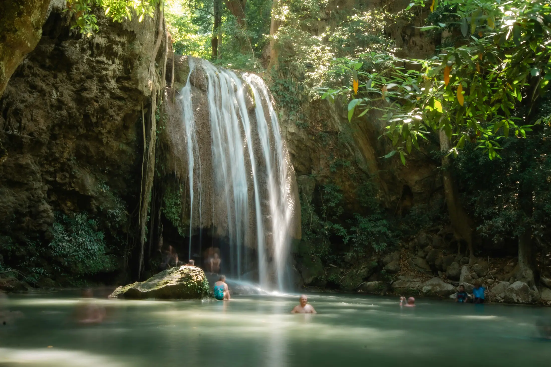 Visitors swimming below a tier of Erawan Falls in Kanchanaburi