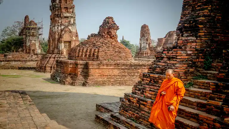 Monk walking beside brick temple ruins in Ayutthaya